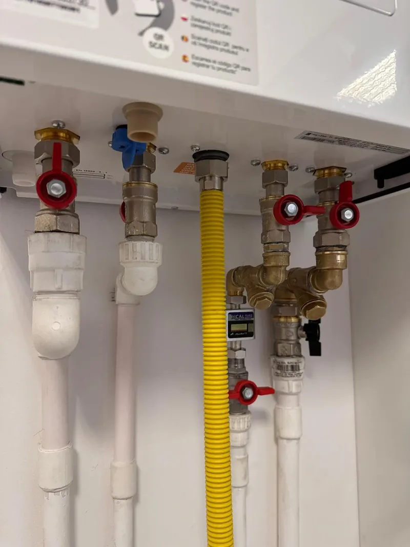 Racorduri noi sub o centrală termică: robineți roșii, țeavă de gaz galbenă, țevi albe de apă